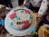 Man sieht einen großen runden Kuchen mit einer weißen Zuckerschicht, hellblauen Blüten und rosafarbenen Schmetterlingen. In Schokobuchstaben steht darauf geschrieben: Schulfest 2017.