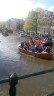 Auf einem Kanal (Gracht) in der Stadt fahren Boote auf denen viele Menschen stehen und feiern. Alle tragen etwas Oranges