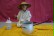 Ein kleiner Junge, als Chinese verkleidet mit Hut, sitzt auf einer gelben Decke und hält Essstäbchen in der Hand.