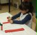 Ein Mädchen klebt chinesische Schriftzeichen auf einen roten Pappstreifen.