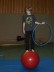Ein Junge steht auf einem großen roten Ball und hält in der linken Hand einen Gymnastikreifen.