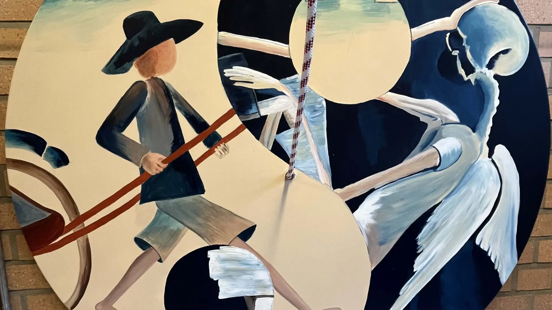 Ein kreisförmiges Kunstwerk an einer Ziegelwand, das das Yin-Yang-Symbol als Bühne für eine Szene über Leben und Tod nutzt: Links zieht ein Mensch einen Karren auf hellem Grund, rechts steht eine skelettartige Engelsfigur auf dunklem Grund.