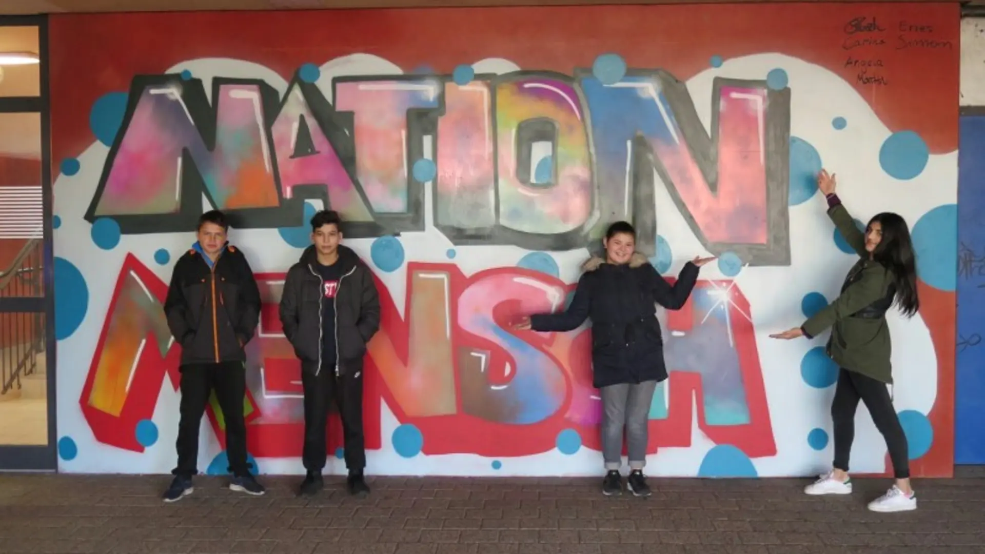 Buntes Gemälde des Maskottchens der Schule: ein fröhliches Flusspferd, dass die Arme in die Luft reckt. Es scheint zu tanzen. Es trägt ein Kleider das der Nationalflagge von Mazedonien entspricht.