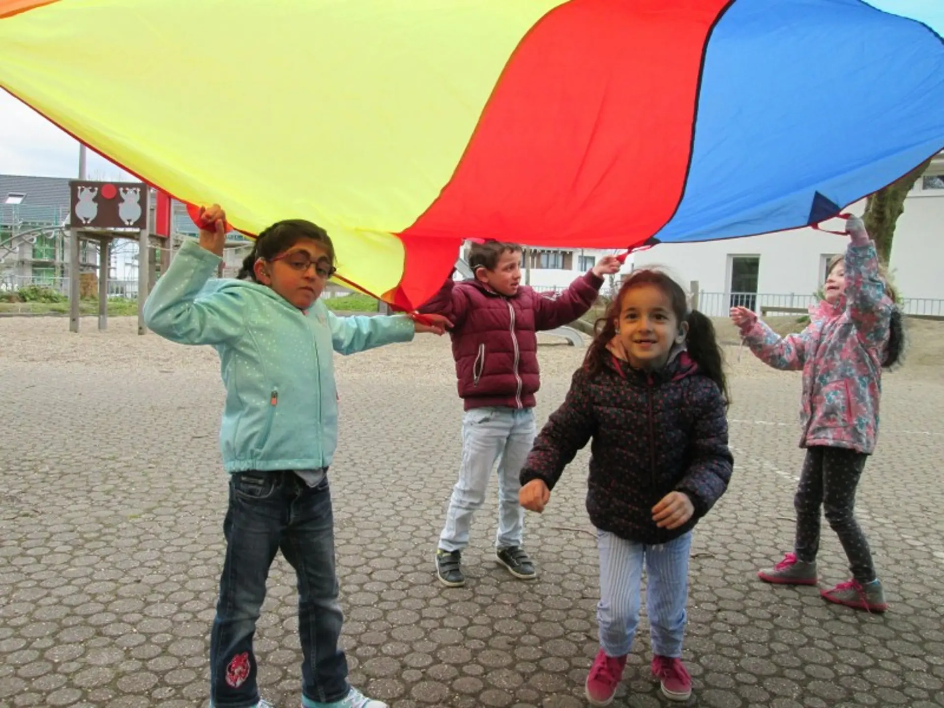 Vier Kinder spielen im Freien unter einem bunten Zelt-Tuch.