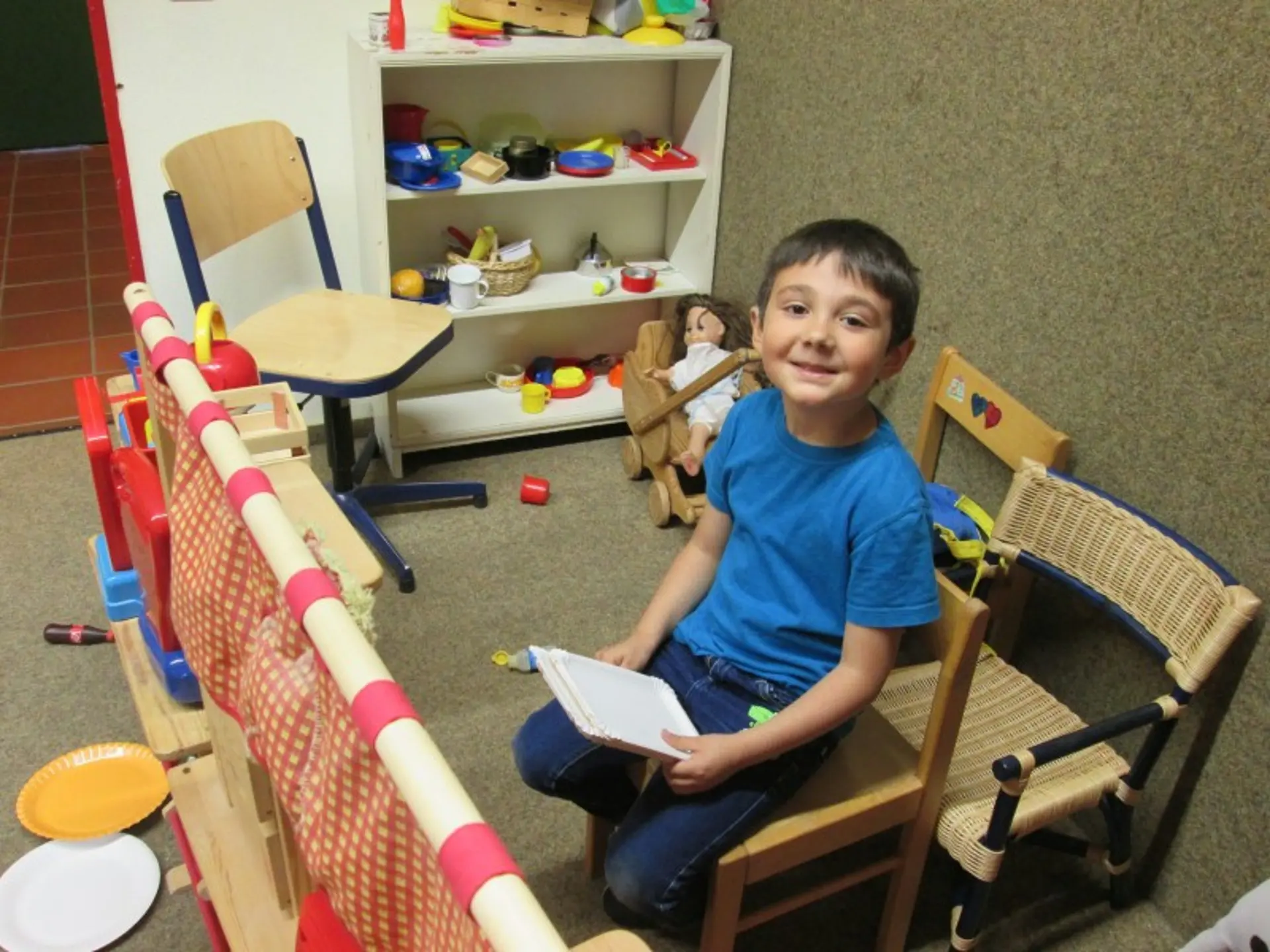 Ein Junge sitzt auf einem Stuhl in einer Spiel- oder Puppenecke.